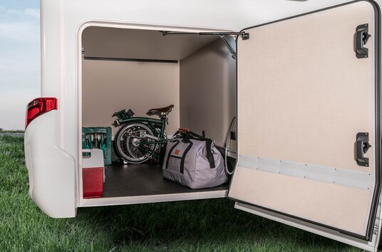 The HYMER motorhome's rear garage is open and loaded with a folding bike, water box and other items of luggage