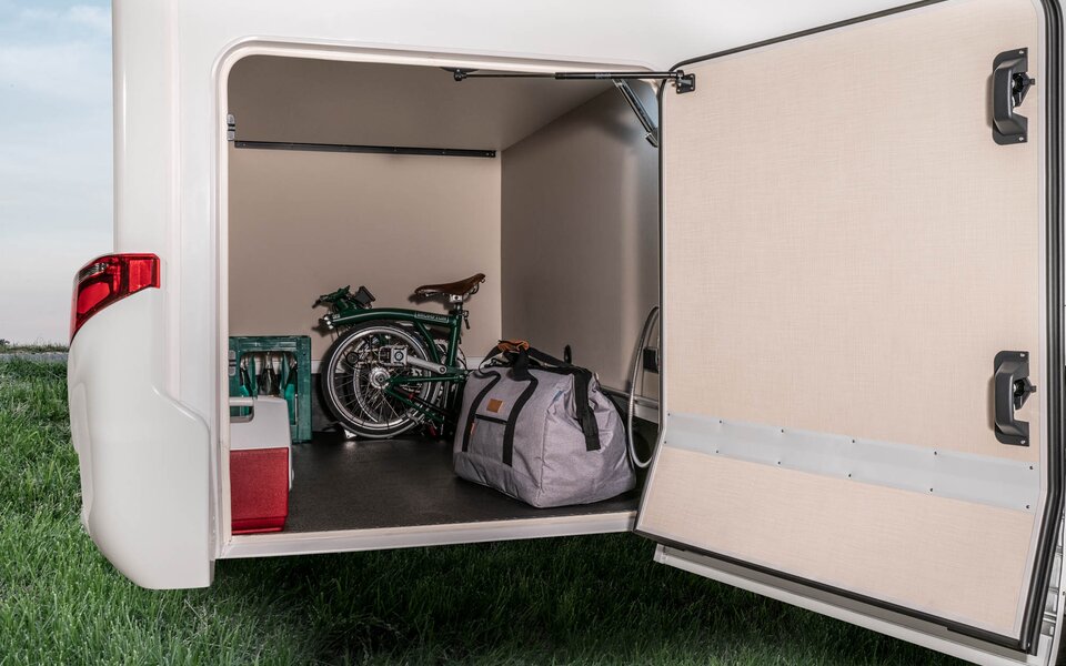 The HYMER motorhome's rear garage is open and loaded with a folding bike, water box and other items of luggage