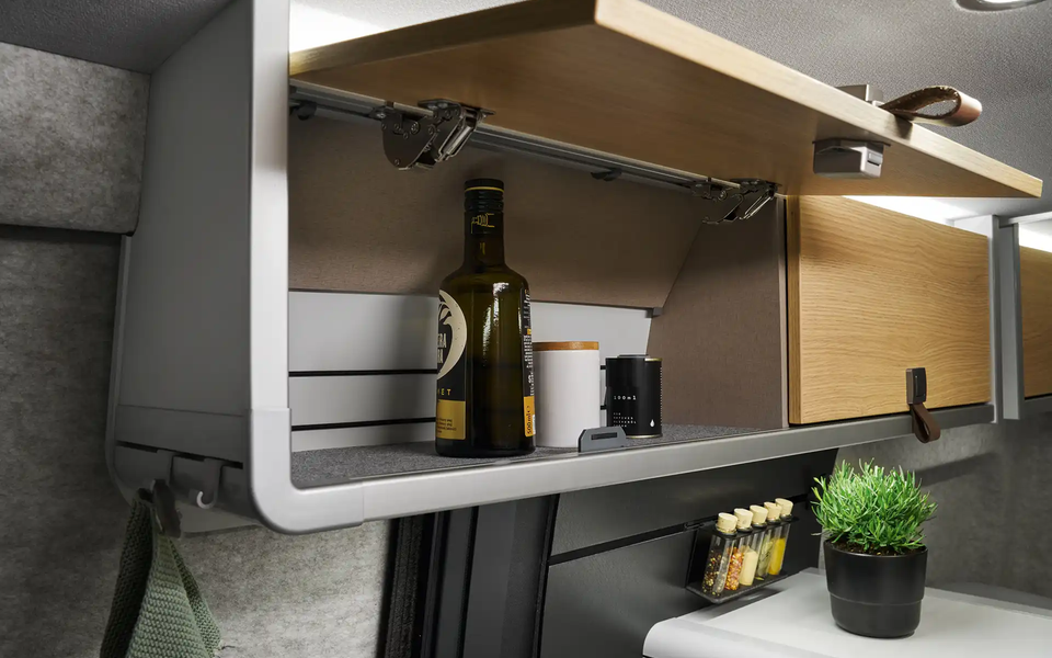 Der Dachstauschrank über der Küche des HYMER Grand Canyon S in der Stilwelt Pearl Grey ist geöffnet. Es sind Öl und Gewürze darin zu sehen.