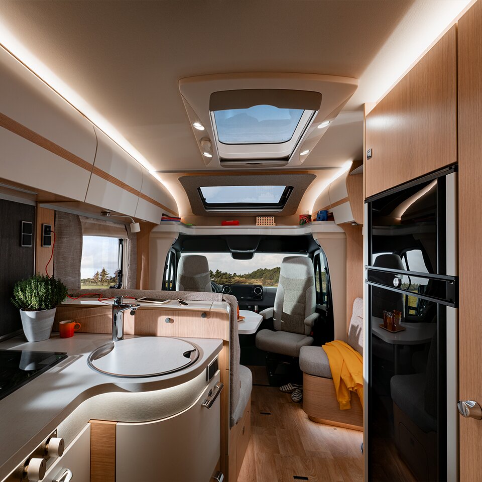 Blick auf Küche und Sitzgruppe des HYMER B-Klasse MasterLine T, durch die Frontscheibe ist Natur zu sehen. Auf der Sitzbank liegt eine gelbe Jacke.