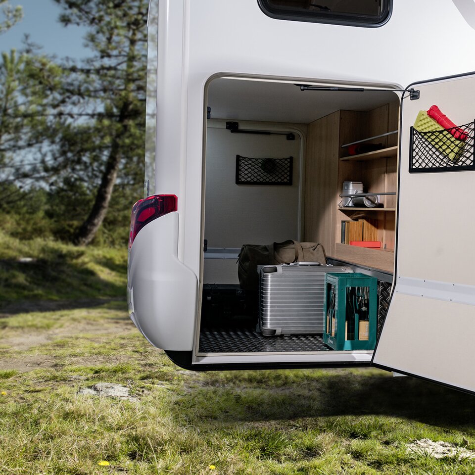 Die Garage des Mercedes HYMER B-Klasse Modern Comfort T ist einseitig geöffnet, darin stehen Koffer, Tasche, ein Getränkekasten und weiteres Zubehör.