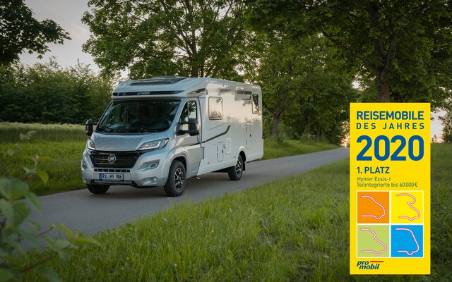 HYMER Exsis-t drives on the road lined with green meadows and trees / with the award Motorhome of the Year 2020