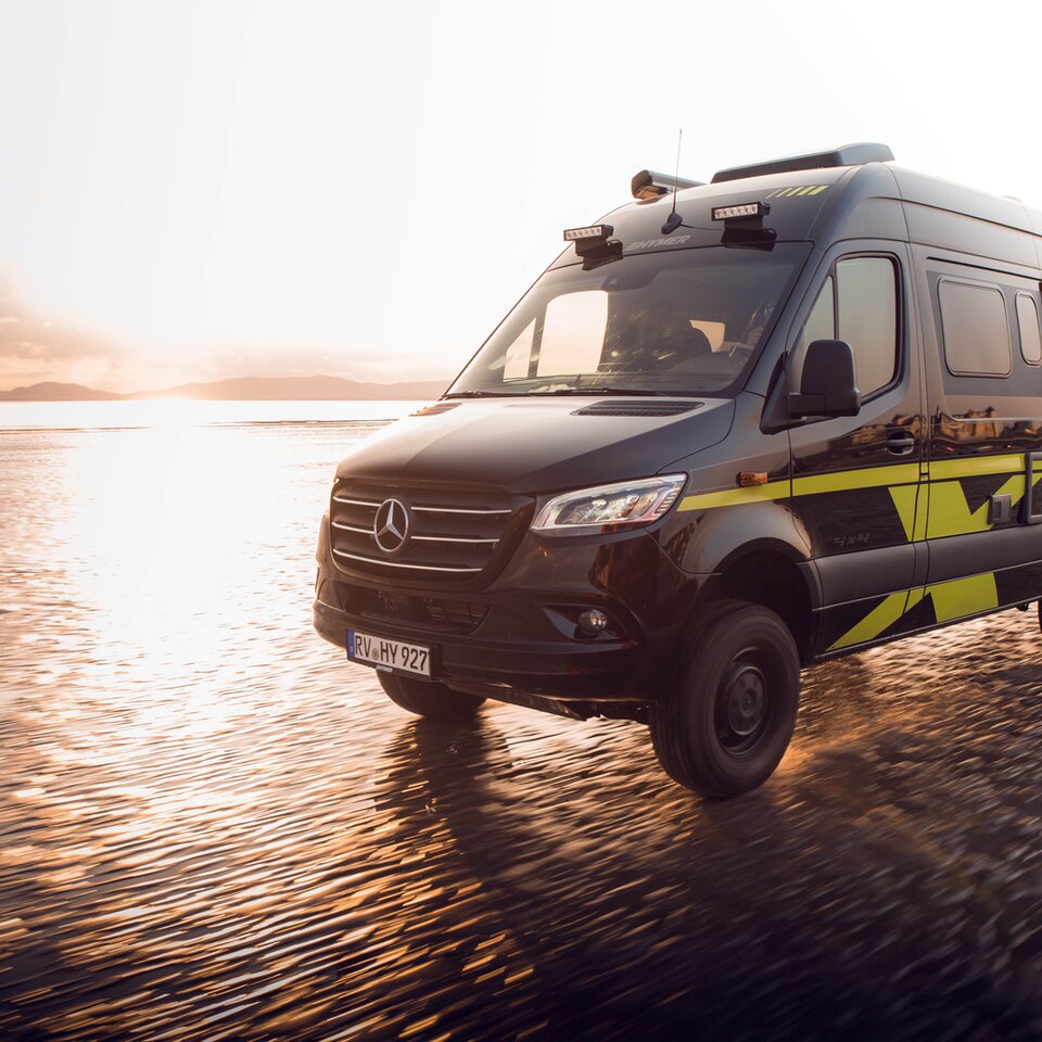 Il camper Mercedes Sprinter HYMER Grand Canyon S viaggia velocemente su una spiaggia soleggiata e bagnata. L'ambiente è sfocato per via della dinamica.