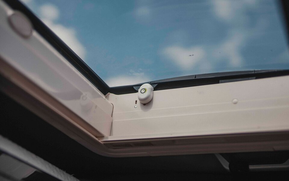 Close-up of a motorhome roof window with a sensor attached. The blue sky is visible in the background.	