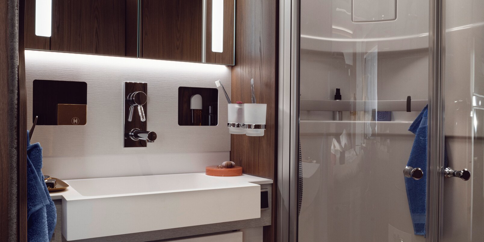 HYMER B-ML I 890:n ylellinen kylpyhuone: valaistu peilikaappi, säilytystilaa pesualtaan alla sekä erillinen suihku lasiovilla
