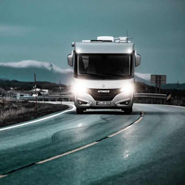 Illuminated, moving HYMER B-ML I motorhome on a slippery Atlantic road at dusk