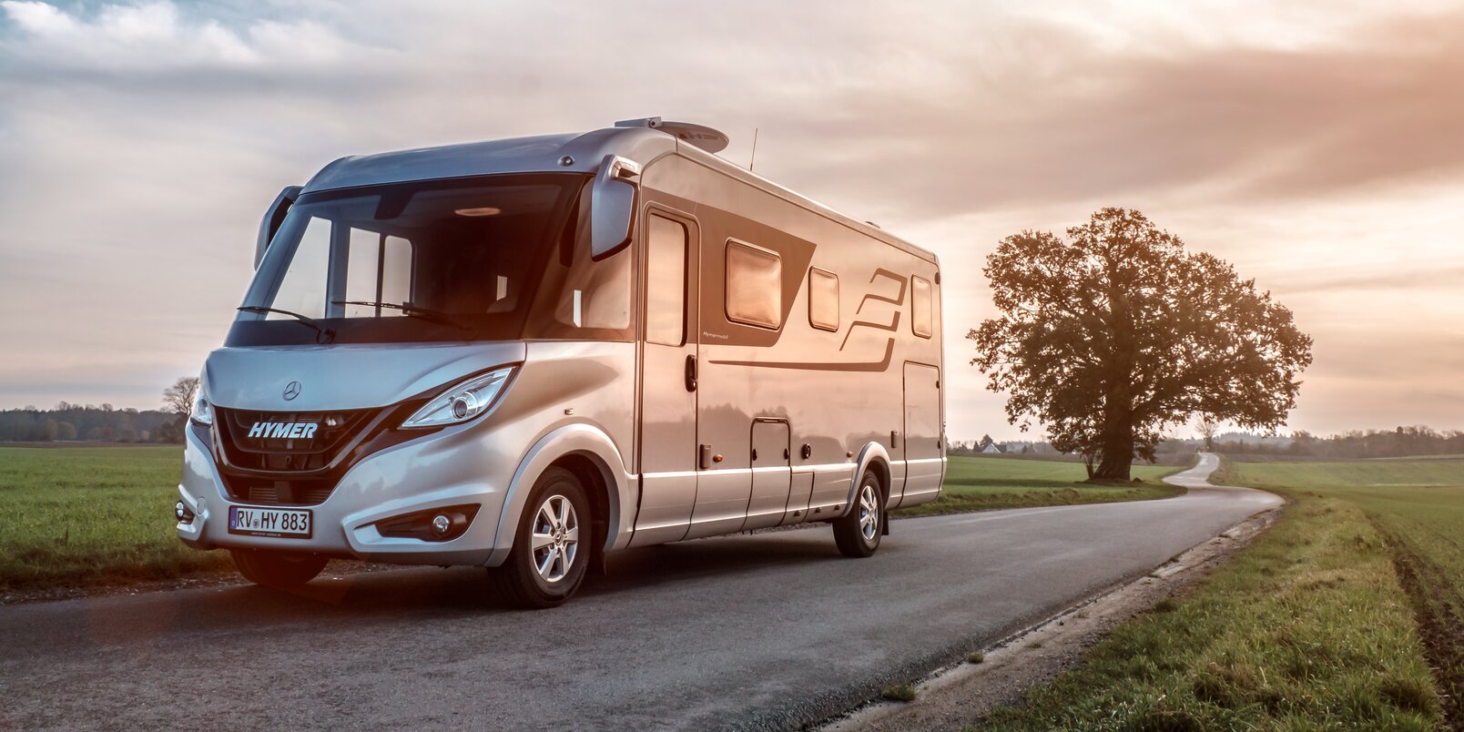 HYMER B-Class Masterline on the road in a flat landscape with green meadows and trees