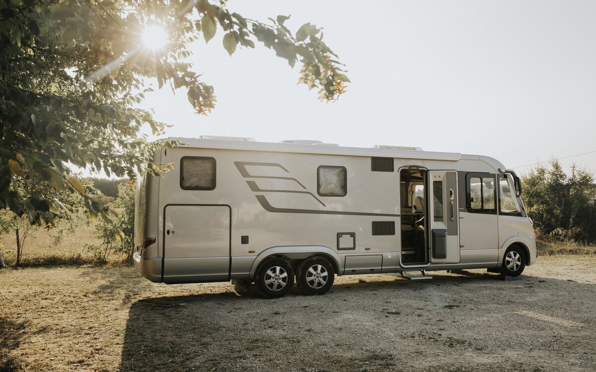 HYMER B-Class MasterLine I parked at the edge of the field with the body door open as a double-axle vehicle in a warm mood lighting