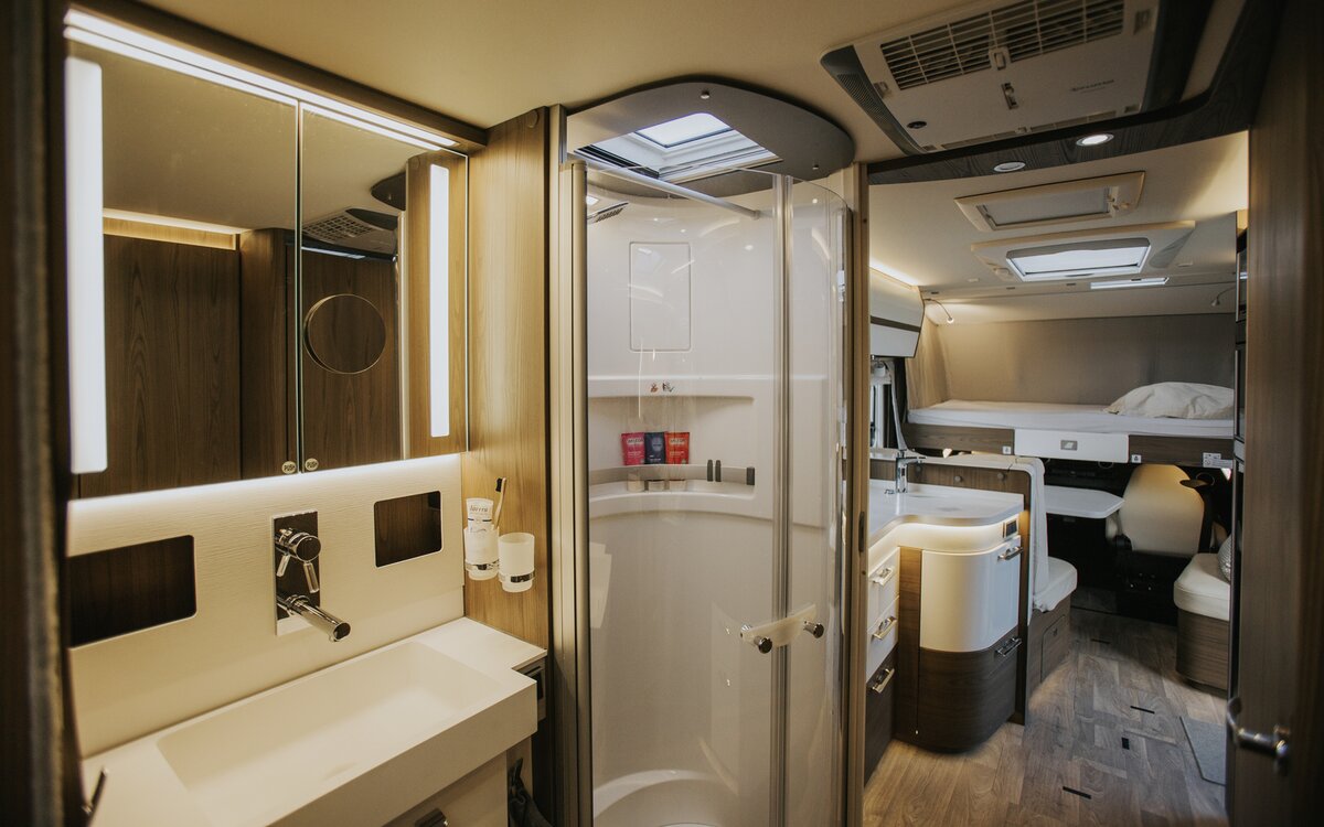 Interior of a camper van with a large saloon bathroom, separate shower, kitchen and drop down bed in the background