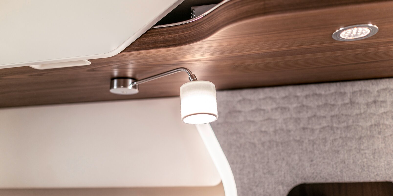 Lámpara de lectura con brazo plateado y pantalla blanca en la zona de la cama de la autocaravana HYMER Clase B MasterLine I