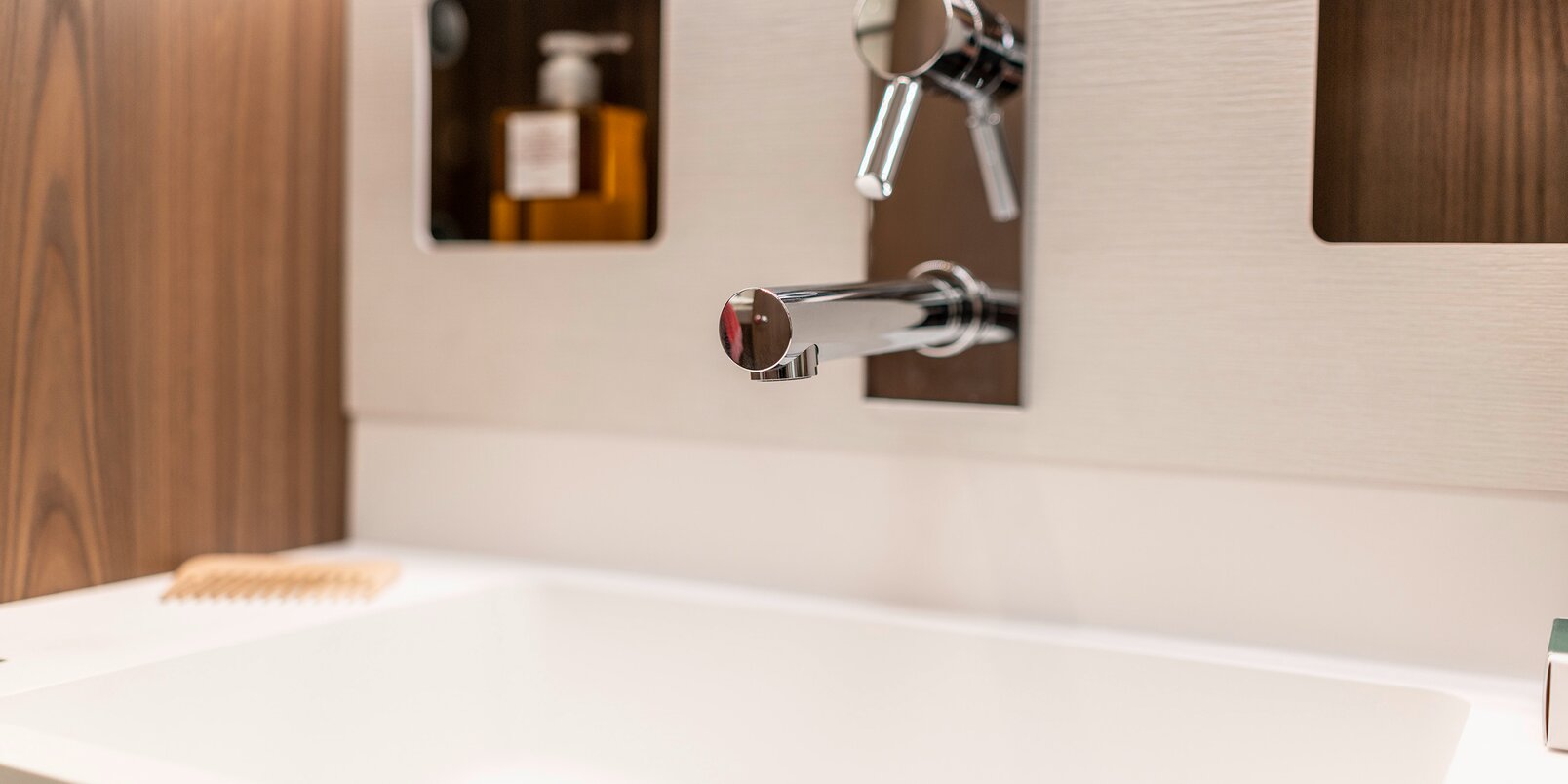 Lavandino design con rubinetto integrato, spazi d’appoggio e rubinetteria sulla parete del bagno di tipo salone nell’HYMER classe B MasterLine 