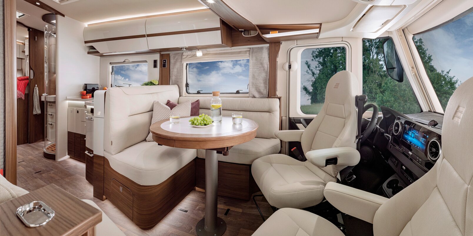 Living room in the HYMER-B-MasterLine with a round table and seating in cream-colored leather