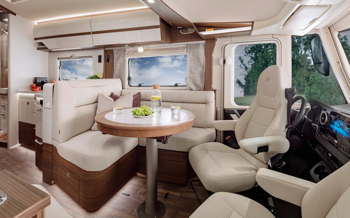 Living room in the HYMER-B-MasterLine with a round table and seating in cream-colored leather