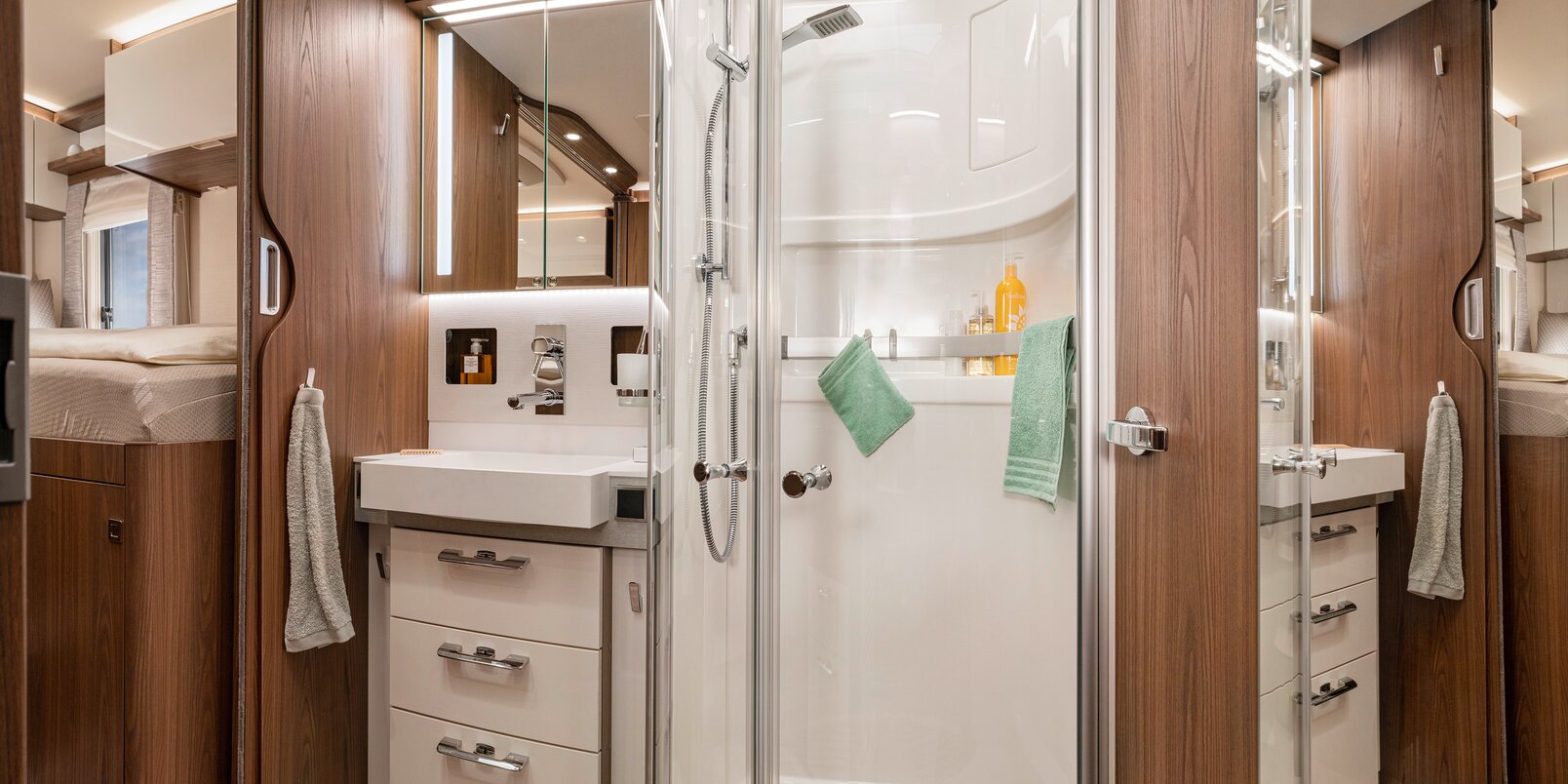HYMER B-ML I 880:n ylellinen kylpyhuone: peilikaappi, säilytystilaa pesualtaan alla, erillinen suihku lasiovilla sekä kylpyhuonetarvikkeita