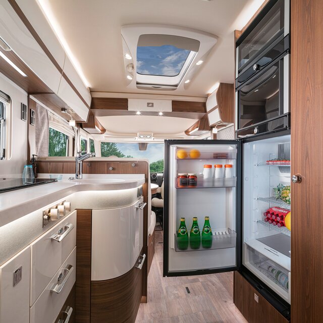 Filled, open refrigerator opposite the kitchen work surface in the HYMER B-ML I 880