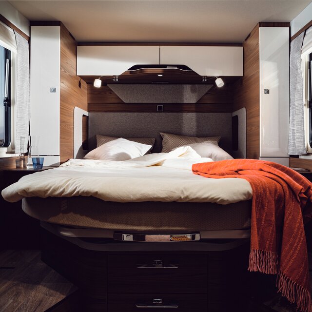 Queen-size bed with cream-colored bed linen and red decorative blanket in the rear of the HYMER B-ML I 890