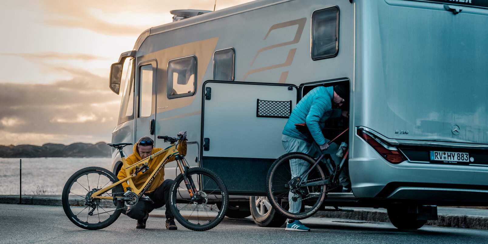 Two men loading mountain bikes into the rear garage of the HYMER B-Class MasterLine