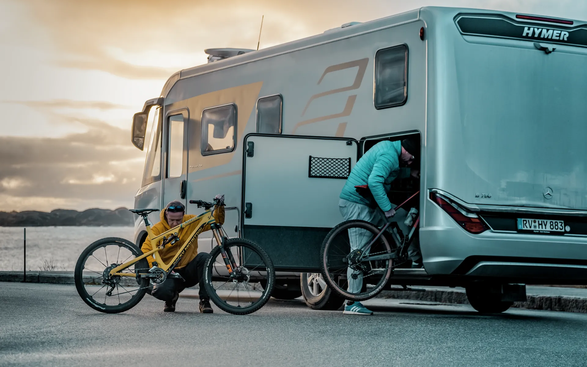 Two men loading mountain bikes into the rear garage of the HYMER B-Class MasterLine