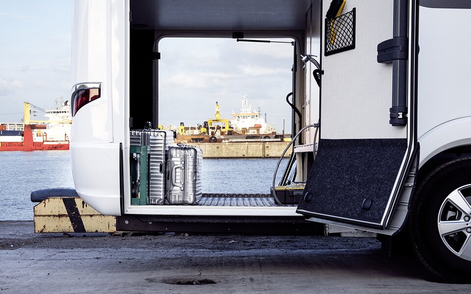 I den åbne garage på HYMER B-Klasse Master Line I, en autocamper med Mercedes-førerhus, står der kufferter. I baggrunden ses der en havn.