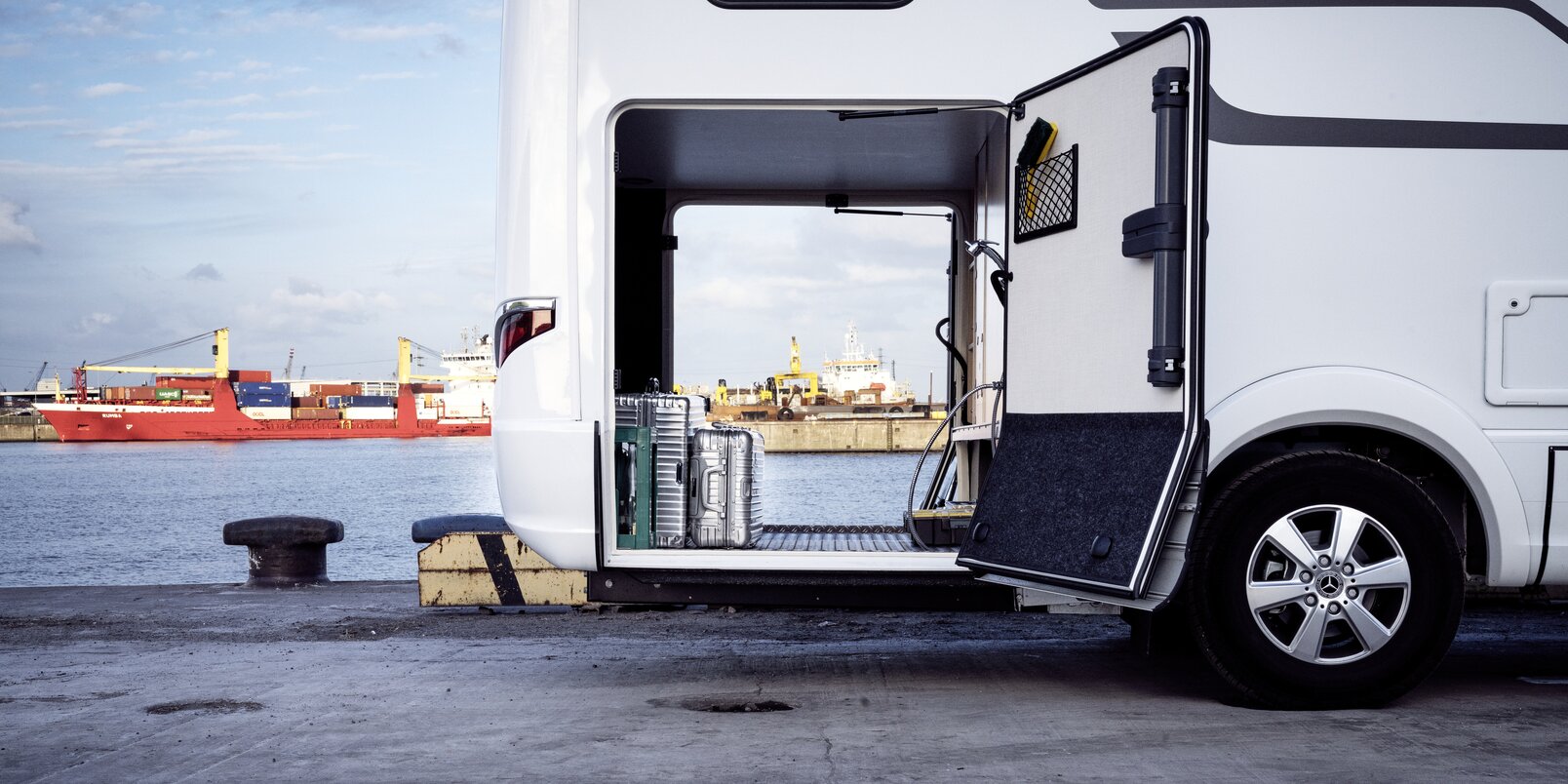View through the rear garage of the HYMER B-Class MasterLine loaded with silver suitcases in front of a port facility