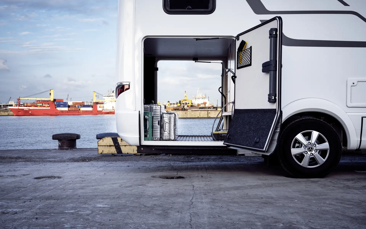 View through the rear garage of the HYMER B-Class MasterLine loaded with silver suitcases in front of a port facility