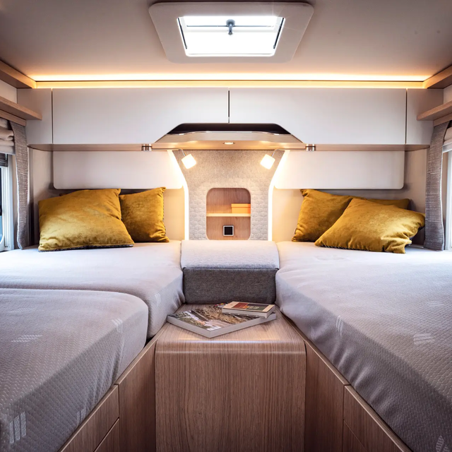 Cosy sleeping area in the rear of a mobile home with two twin beds connected by an additional cushion; two mustard-colored cushions are traped at the head ends