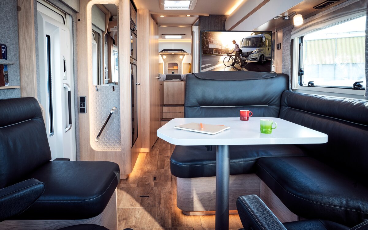 Seating group in black leather look with a laid table and a view of the TV plasma and rear area in the HYMER B MasterLine