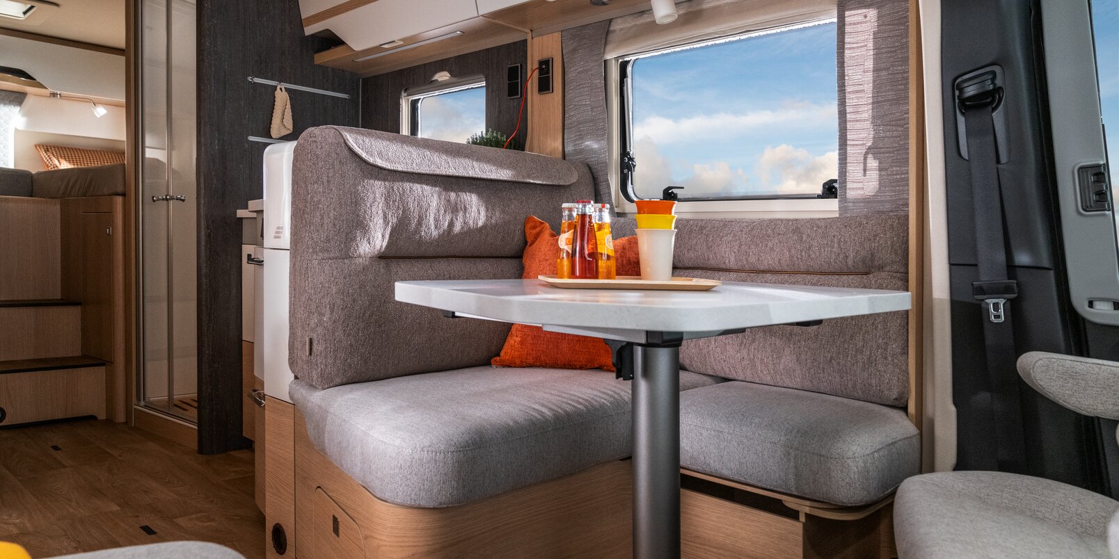 View from the covered seating area and kitchen block through the windows of the HYMER B ML-T 780 of the sunny blue sky
