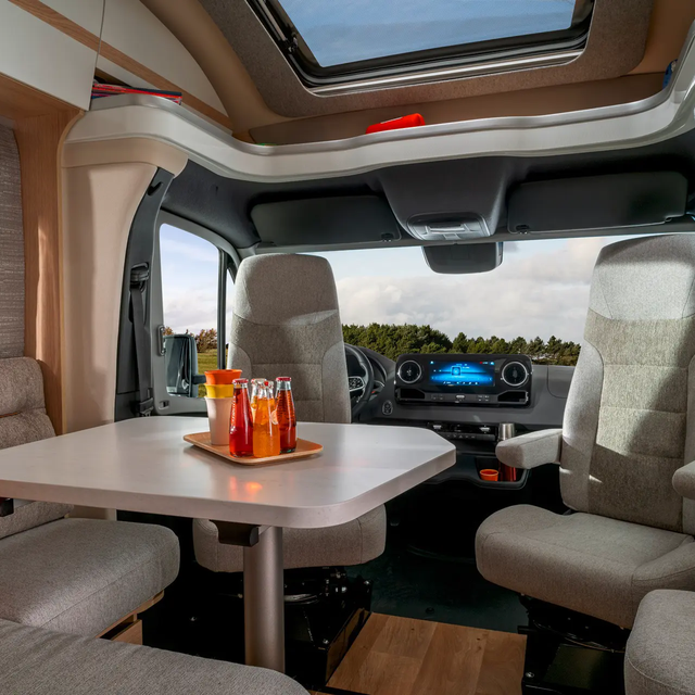 View from the seating group with driver's seats and SatNav in the center console through the window of the HYMER B-ML T to the sky and the forest