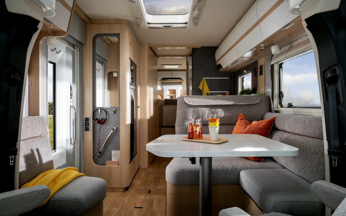 Sideboard entrance door with headphones and covered seating area with orange cushions with a view towards the rear in the HYMER B-ML T