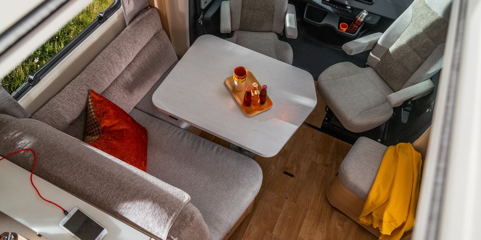 Istuinryhmä kuljettajanistuimilla ja punaisilla tyynyillä sekä matkapuhelin ja aurinkolasit keittiön hyllyllä mallissa HYMER B ML-T 780