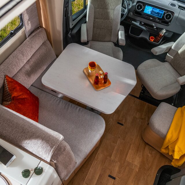 Seating group with driver's seats and red cushions. Plus, a mobile phone and sunglasses on the shelf in the kitchen in the HYMER B ML-T 780