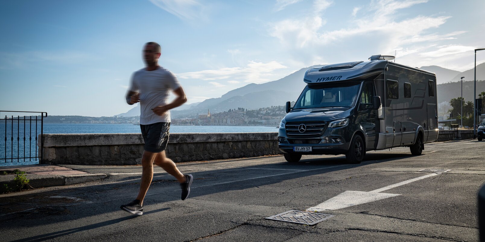 Runners past a parked HYMER MasterLine T on the coast of southern France under a blue sky