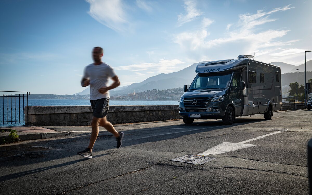 Runners past a parked HYMER MasterLine T on the coast of southern France under a blue sky