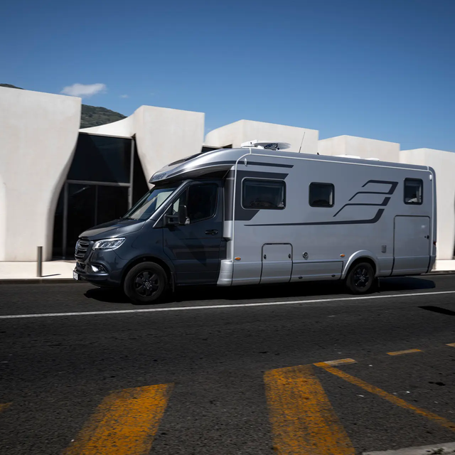 HYMER B MasterLine T in front of a modern white building with large glass facades, blue sky and palm trees