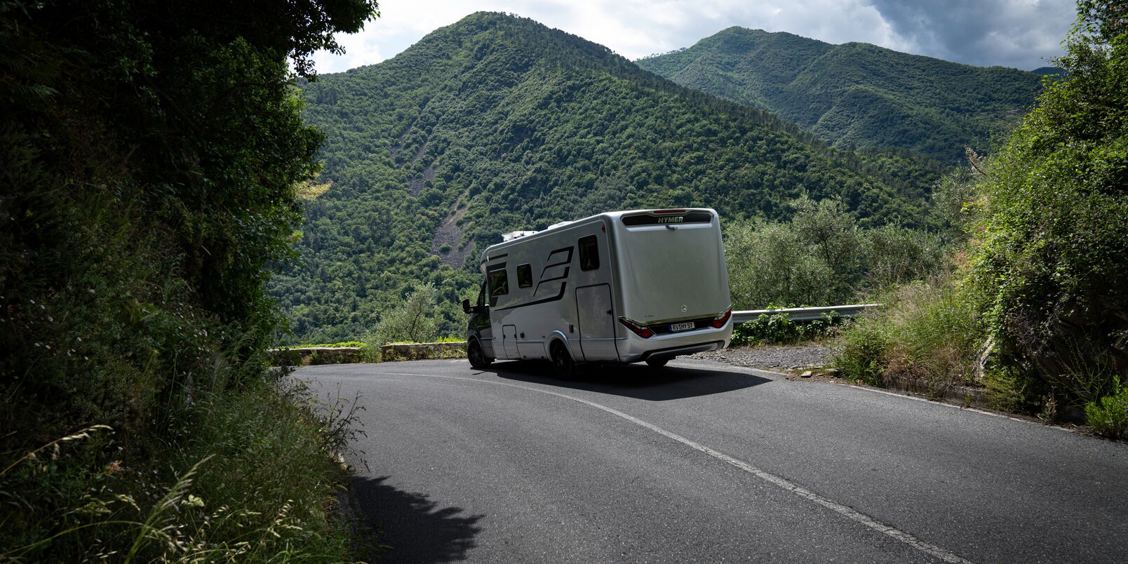 HYMER B-Class MasterLine T motorhome driving downhill in a green mountain panorama with a blue sky