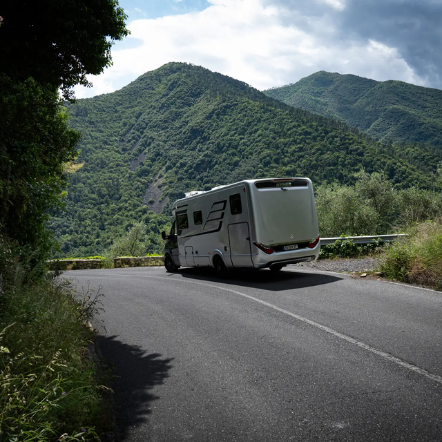HYMER B-Class MasterLine T motorhome driving downhill in a green mountain panorama with a blue sky