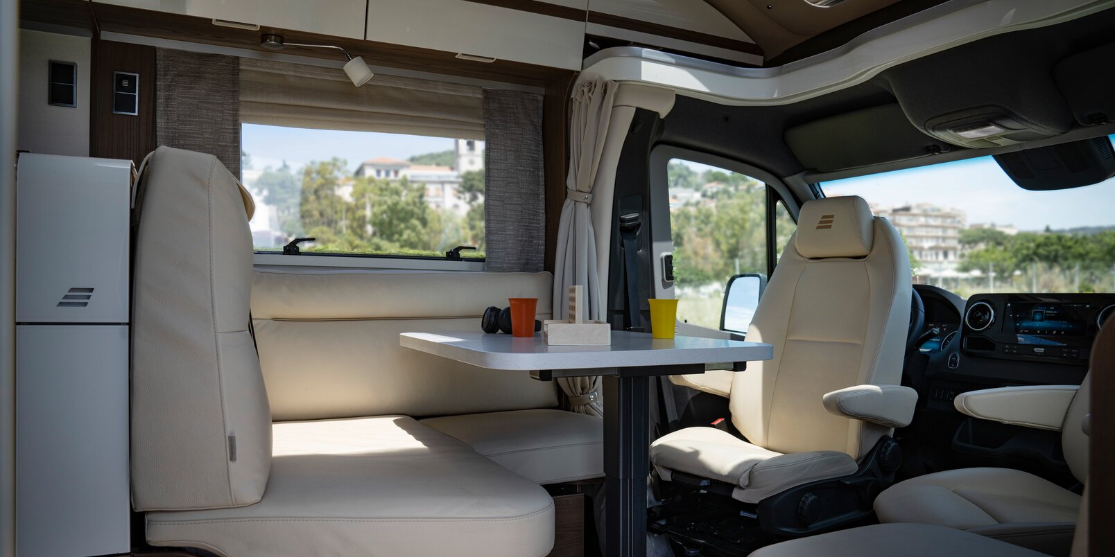 Cream-colored L-shaped seating group in leather look including driver's seats and laid table in the HYMER B-MasterLine