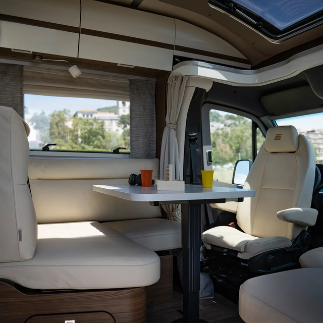 Cream-colored L-shaped seating group in leather look including driver's seats and laid table in the HYMER B-MasterLine