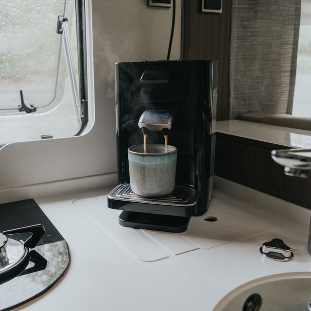 Coffee maker on the kitchen worktop in a mobile home, freshly brewed coffee runs into a gray stoneware mug