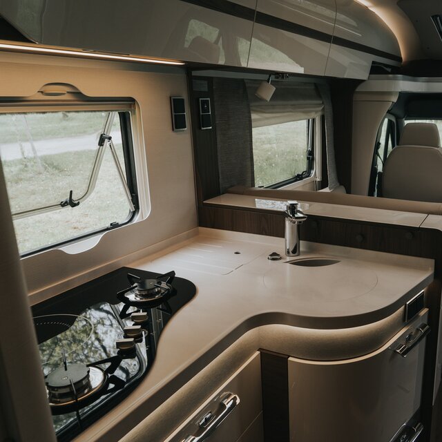 Corner kitchen of a semi-integrated mobile home with hybrid cooker and ambient lighting