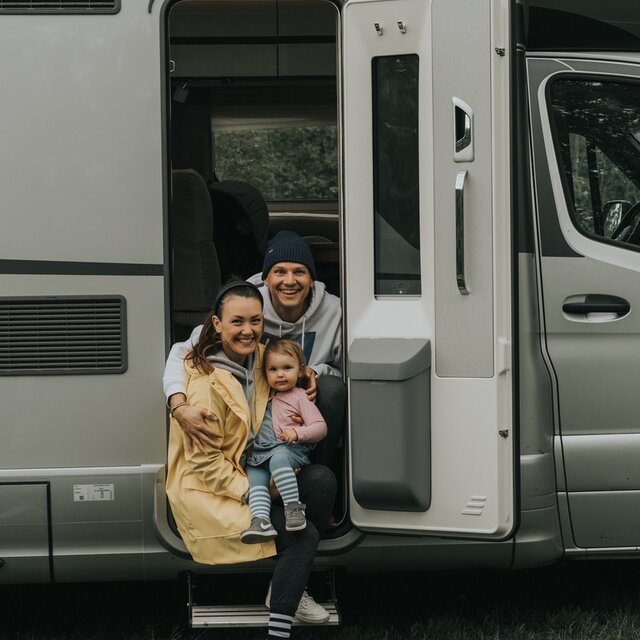 A young couple is sitting with a small child in the open door of a mobile home