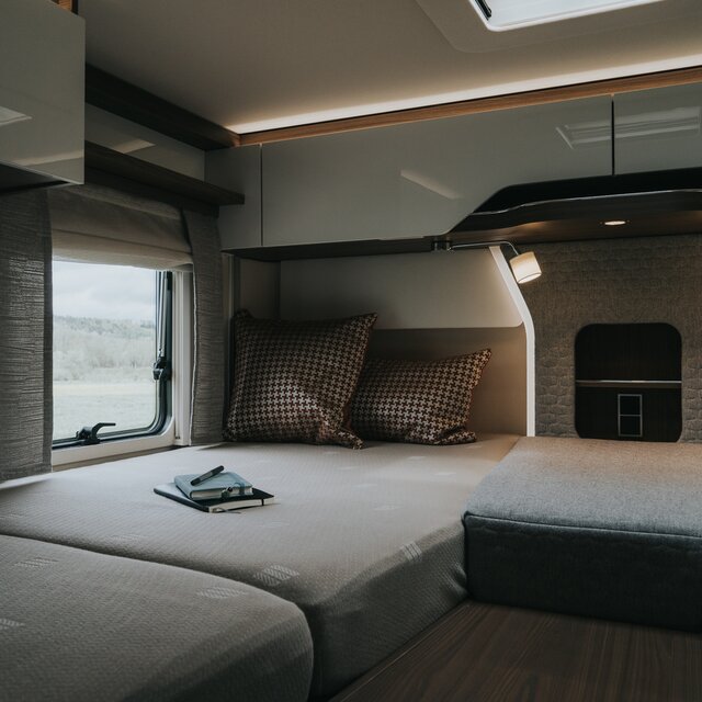 Sleeping area with throw pillows on the bed in the rear of the camper van with the reading lights on and ambient lighting