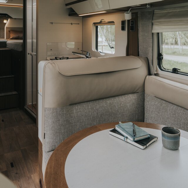 Living area in a mobile home with a light L-shaped seating group and a round table with a real wood frame
