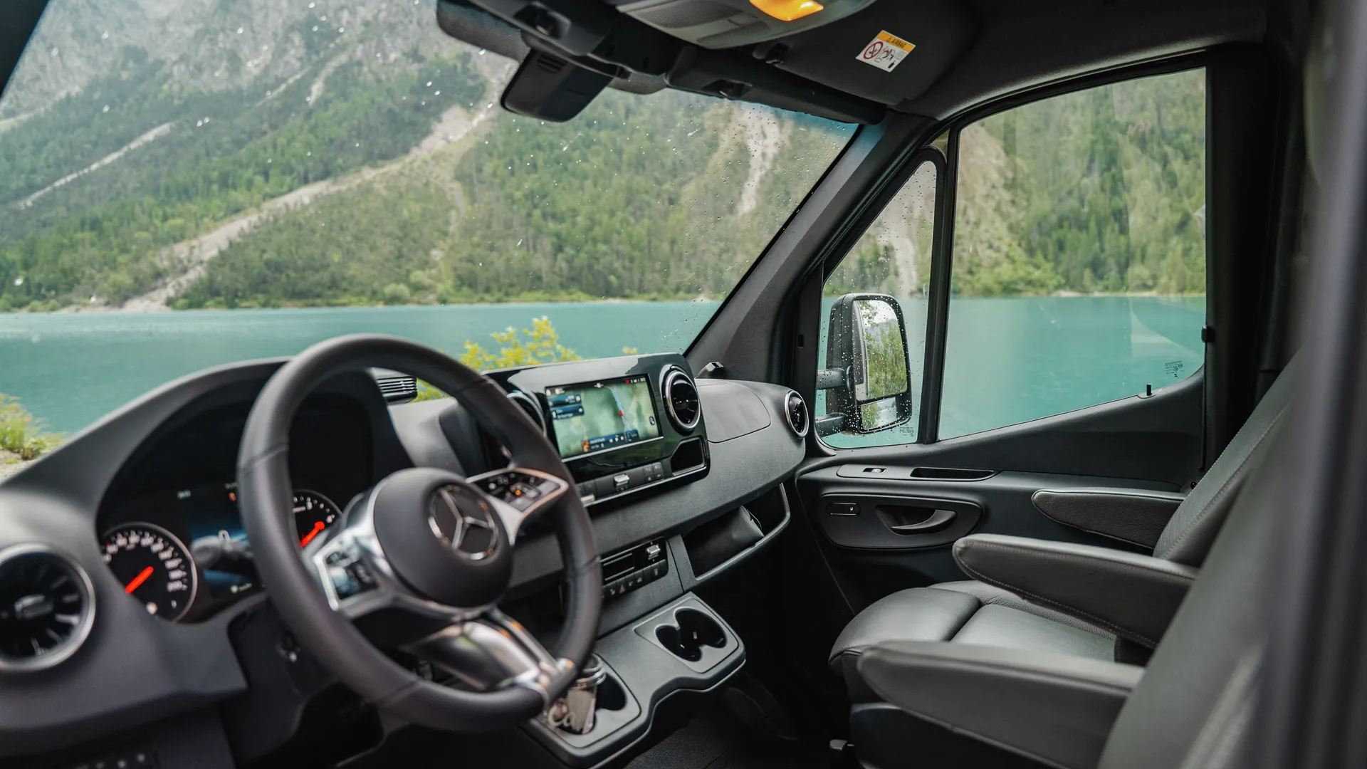 Cab of the Hymer B‑ML T with comfortable captain’s seats, modern cockpit and impressive view of a mountain lake in Alpine scenery