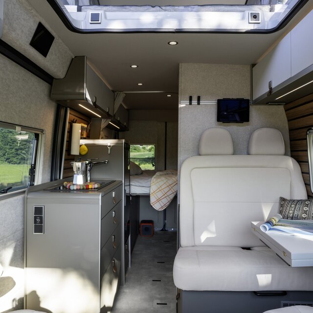 HYMER Camper Van living space: driver's seats, table, bench, kitchen, side wall windows, overhead storage cupboards, rear door with window