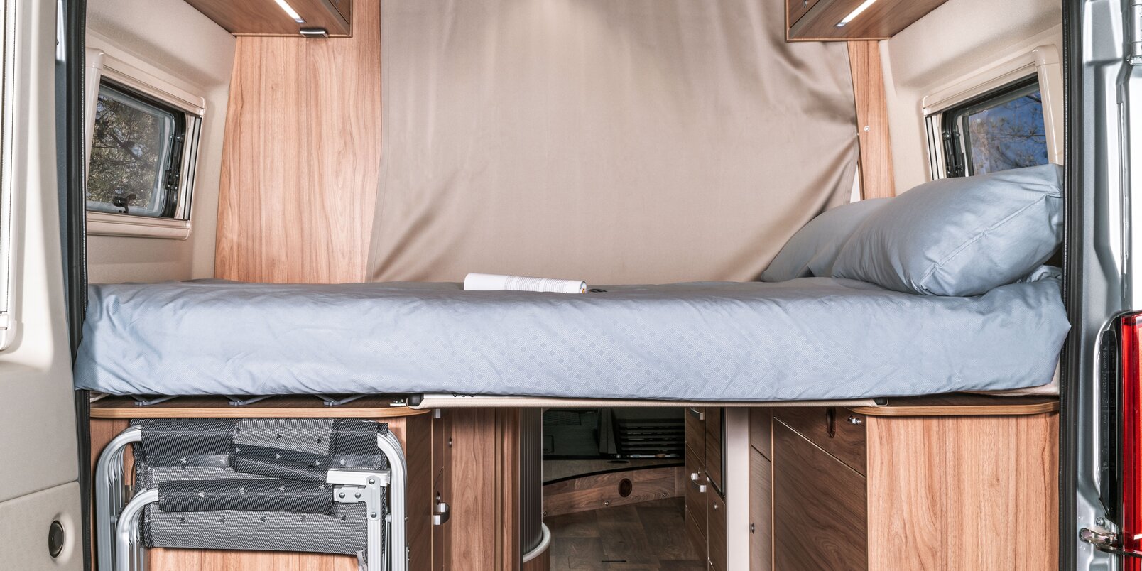 Bezogenes Heckbett, Trennvorhang zum Wohnraum, verstaute Klappstühle im HYMER Camper Van Fiat