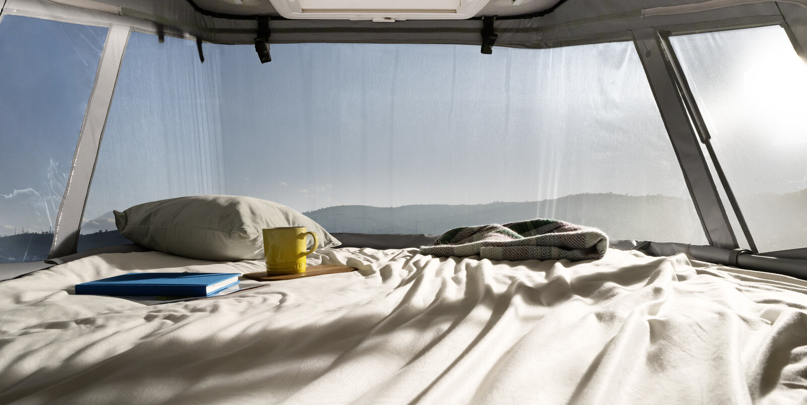 Bezogenes Bett, Kissen und Zeitschrift unterm Aufstelldach beim HYMER Camper Van