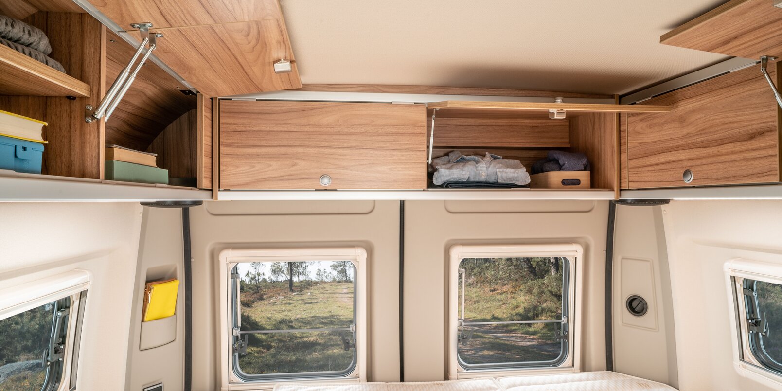 Teilweise geöffnete und befüllte Dachstauschränke über dem Bett-/Liegebereich und Seitenwandfenster im HYMER Camper Van
