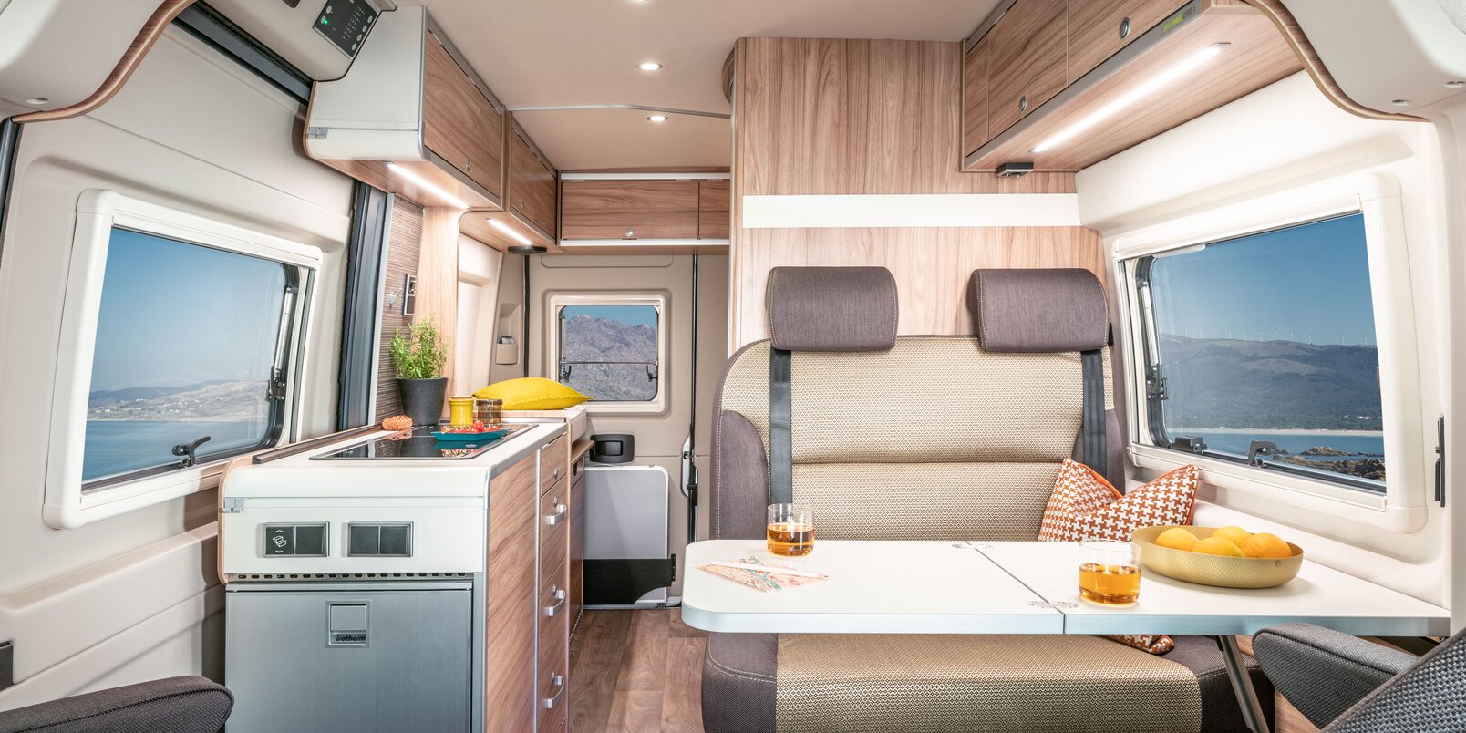 HYMER Camper Van living space: driver's seats, table, bench, kitchen, side wall windows, overhead storage cupboards, rear door with window